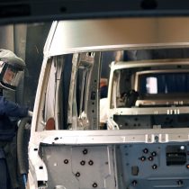 A worker in protective suit and helmet with breathing apparatus sprays metallic paint on a Ford Transit van in the line 2005.