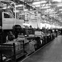 A line of Ford Transits suspended on the monorail production line 1973, men working underneath.